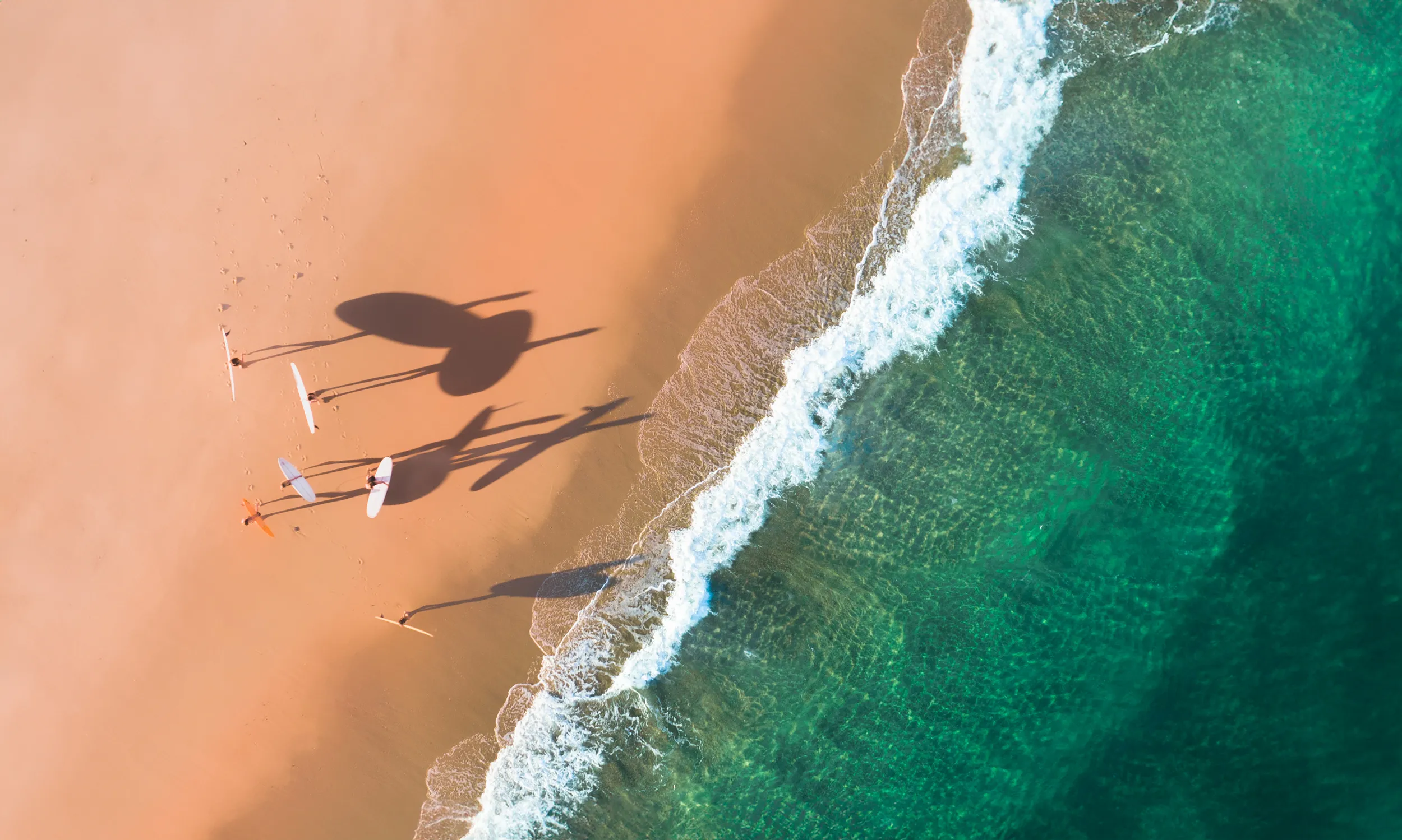 Friends walking across the beach with surfboards in France